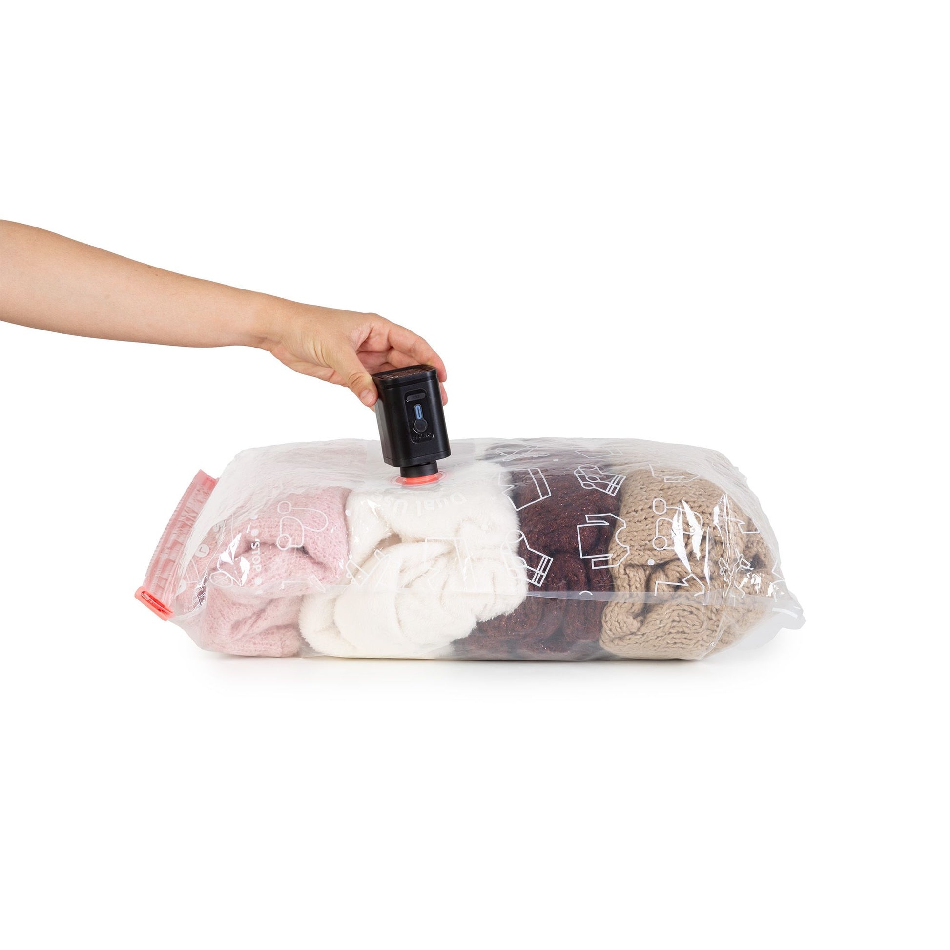 Une main utilisant une pompe pour aspirer l'air d'un des sacs de rangement sous vide rempli de vêtements.